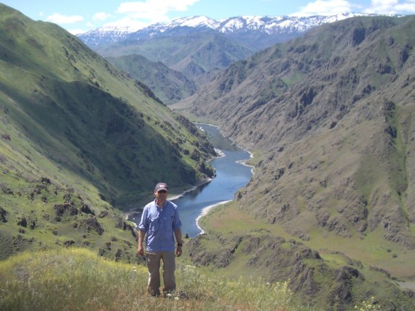 man standing alone on the side of a hill overlooking an expanse of valley and river