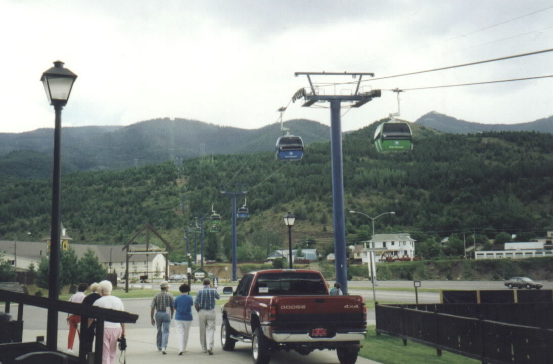 people walking under a green mountain pass below a street sign