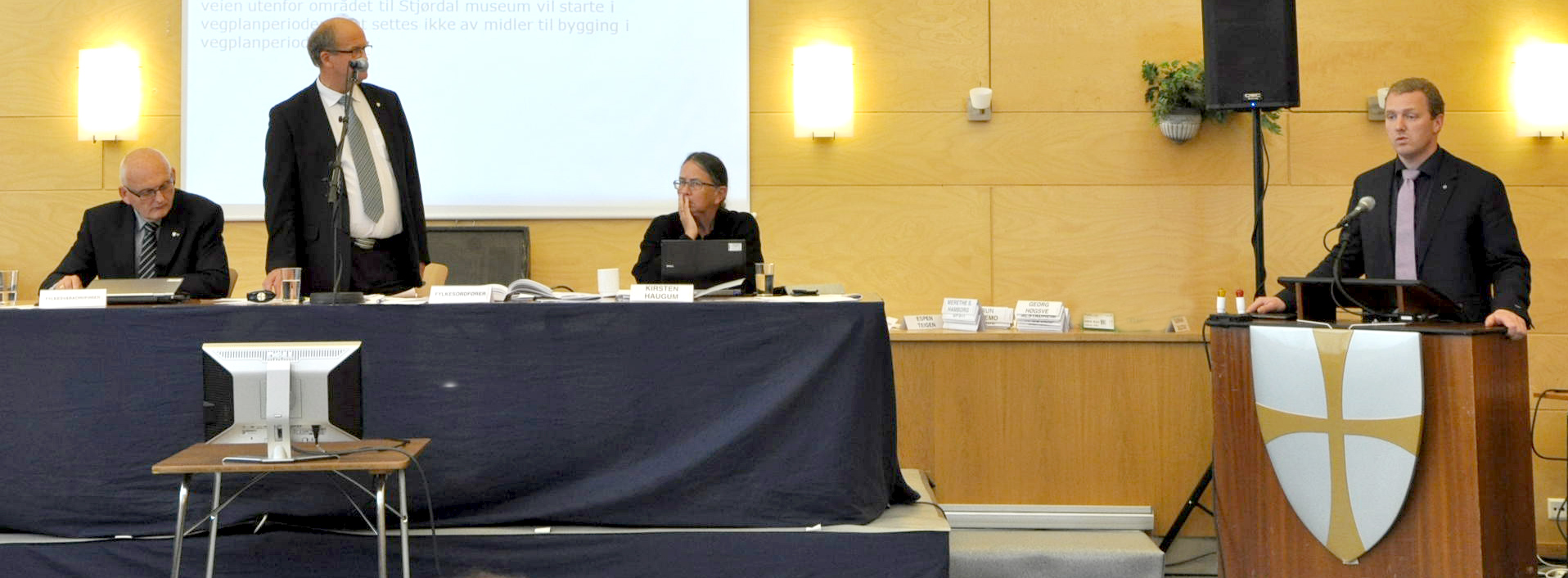 three people are sitting in front of podiums, two people standing