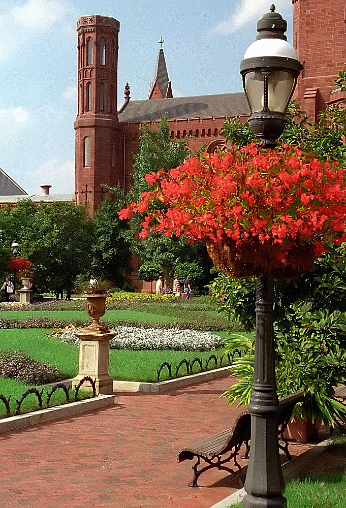 a red brick building with trees and flowers in the foreground