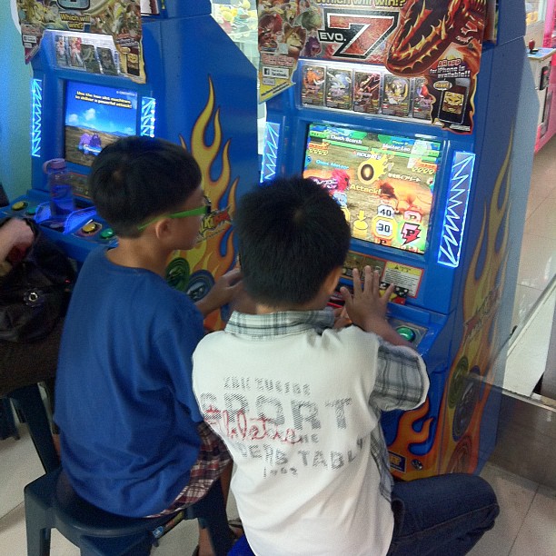 two boys playing with an arcade machine in a mall