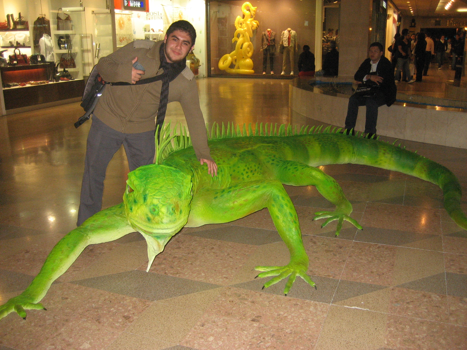 a large green lizard laying on the ground with a man in a brown shirt