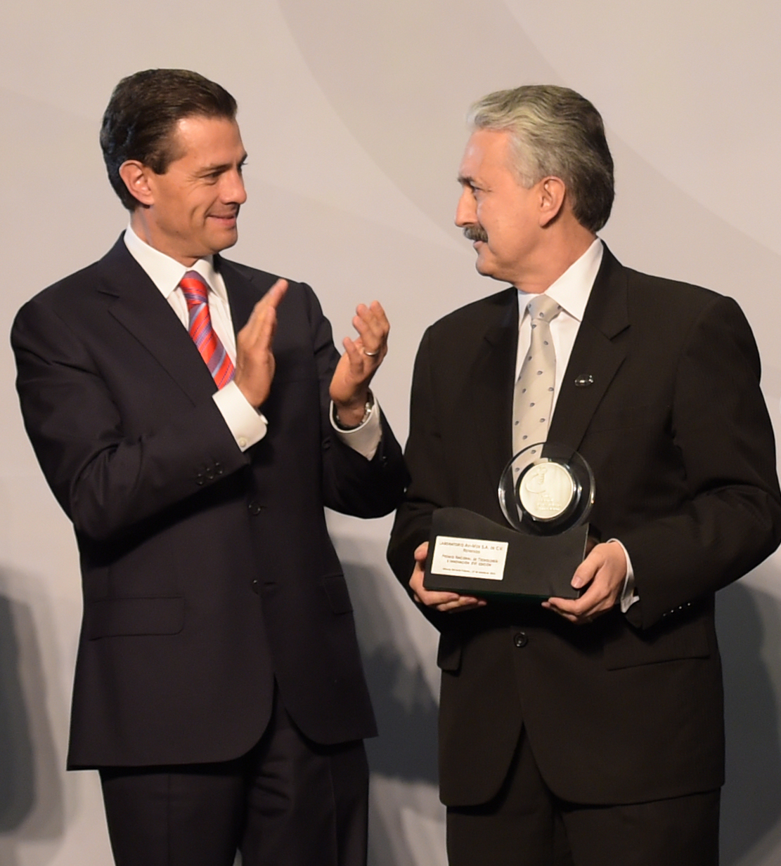 two men in suits are applauding and holding a award