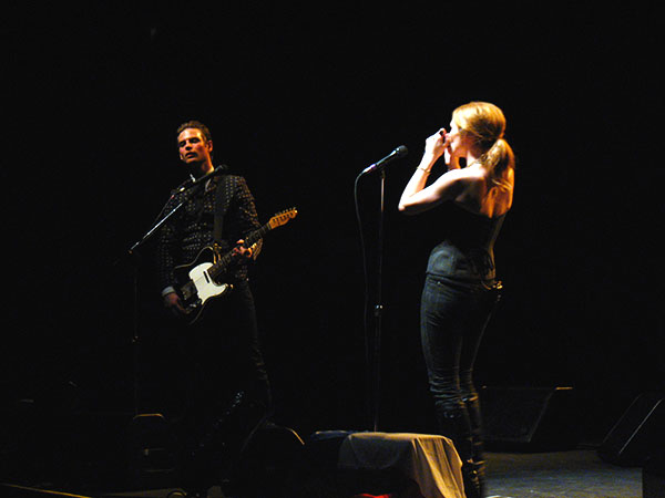 a man and a woman on stage singing while someone plays guitar in the background