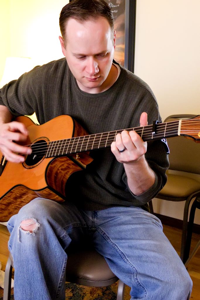 man with guitar sitting on stool in the room