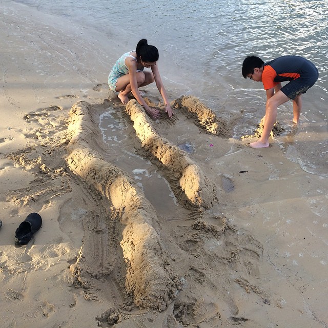 some children and an adult are playing with a sand castle