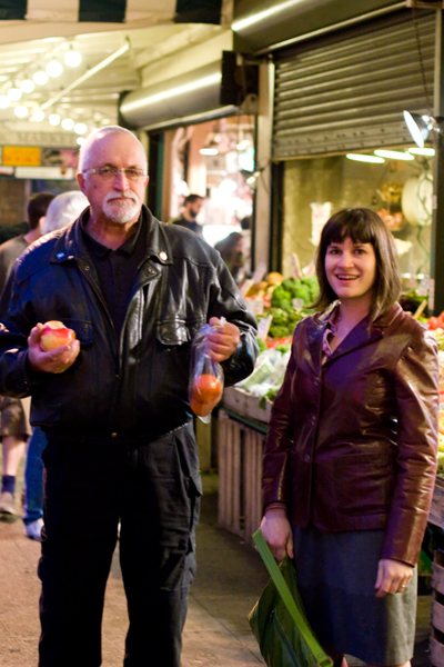 a man and woman standing in front of a fruit stand