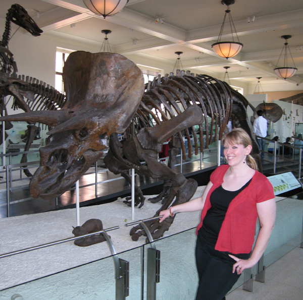 a woman posing in front of a dinosaur skeleton