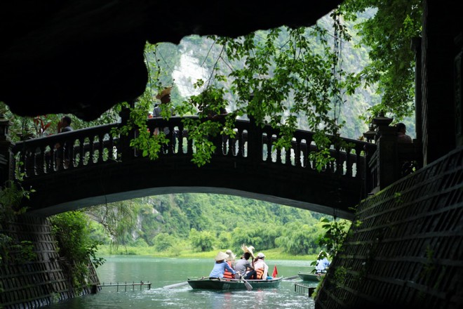 three people in a rowboat on the water under an arched bridge