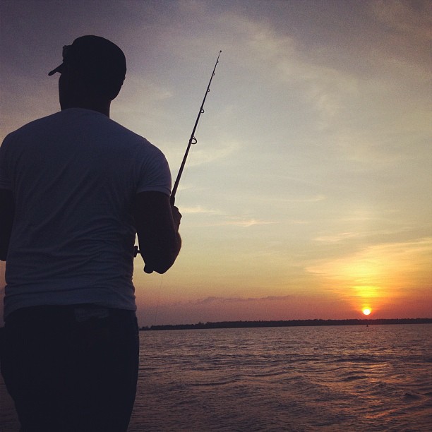 a man fishing in the water at sunset