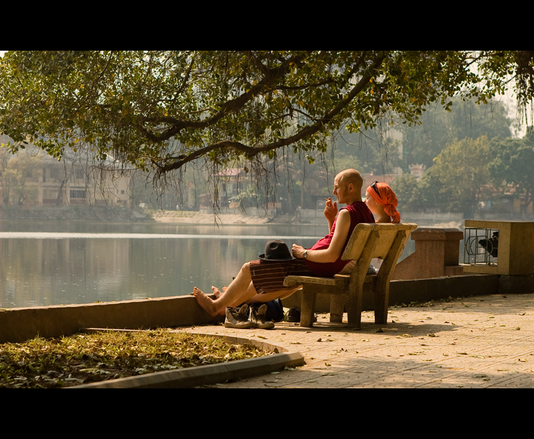 a woman sitting next to a man on a bench near a pond