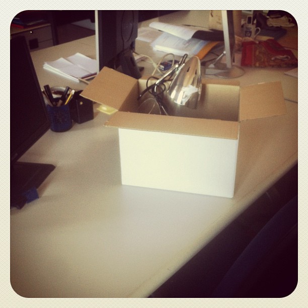 a cardboard box holding scissors and other items on a desk