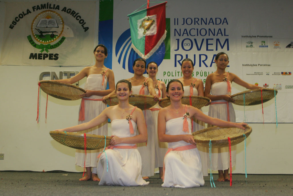 women dressed in white clothes stand on stage holding baskets with flags