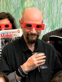 a man has his hands in a drink and wears red glasses