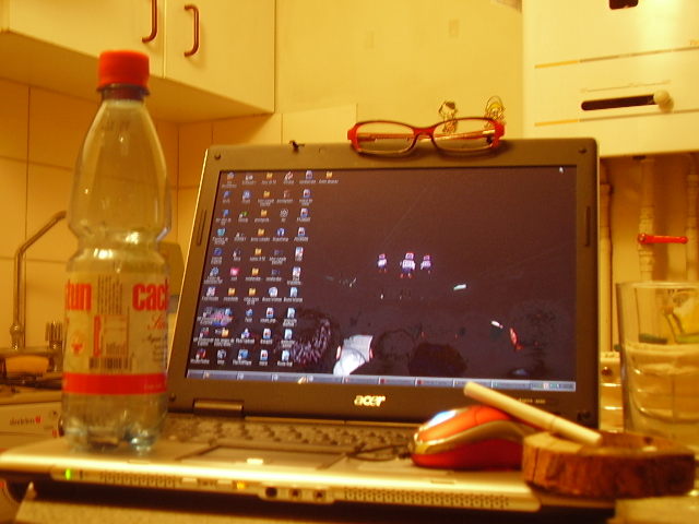 an open laptop and a glass bottle in a kitchen