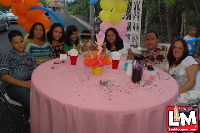 a group of friends sitting at a pink table with some balloons