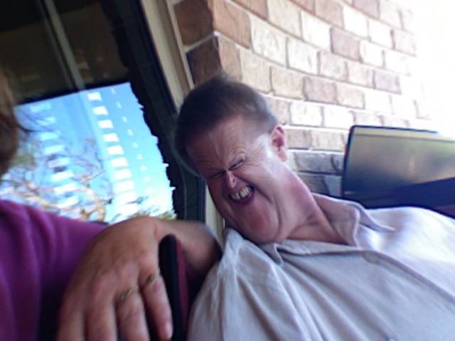 a man laughing while using a phone on a porch