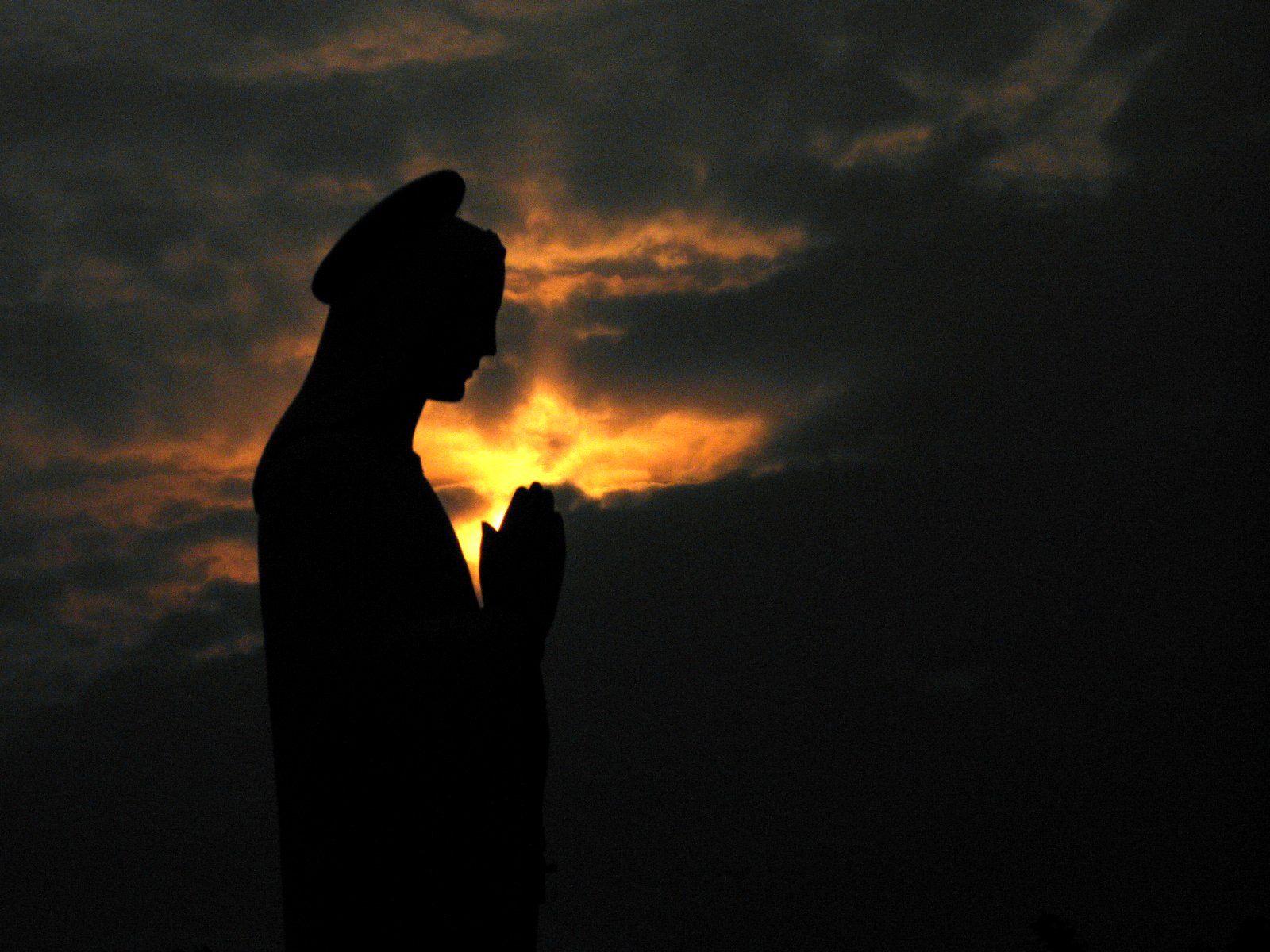 silhouette of a person praying in front of sunset