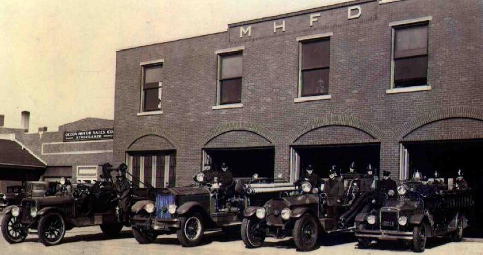 old time fire department cars parked in front of a brick building