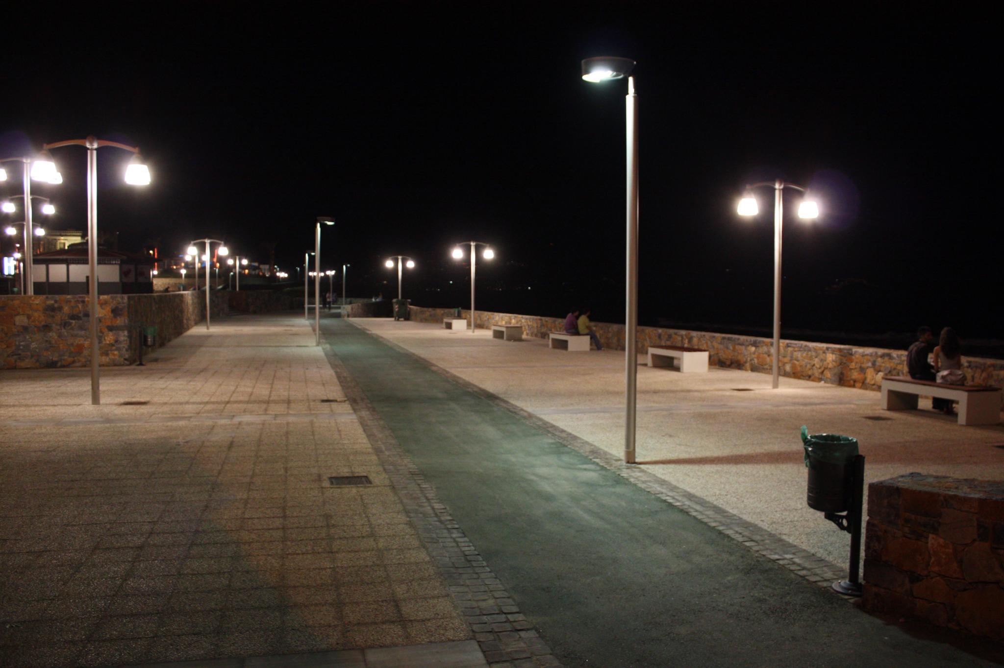 a city street with lights on poles and concrete pavement at night