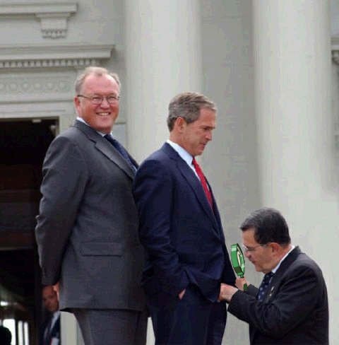 two men shake hands while another man in a suit looks on