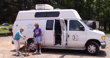 two women are standing next to a van with their dogs