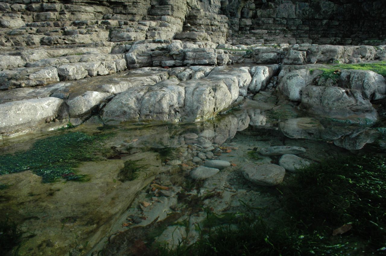 some large rocks and water next to a cliff