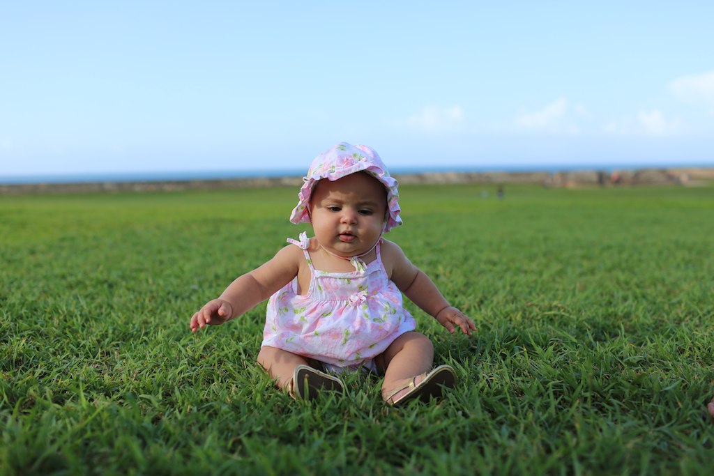 a baby girl sitting on the grass wearing a hat