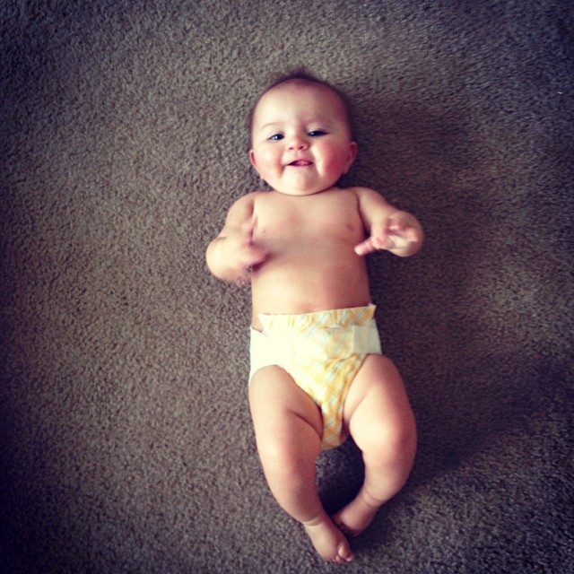 a baby in a diaper smiles on a carpet