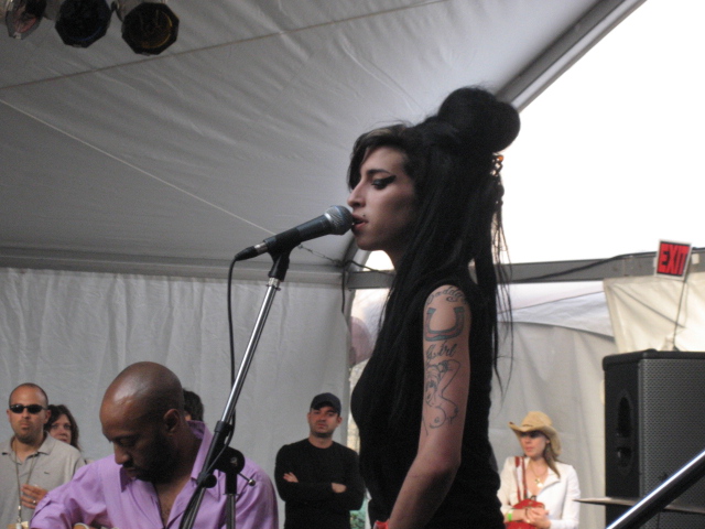 a lady with long hair on stage speaking into microphone and some other people