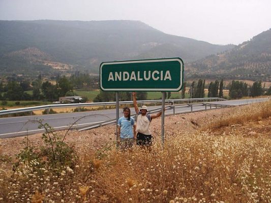 two men standing underneath an antaulouia road sign in the mountains