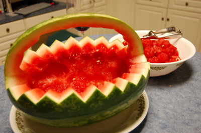 a large watermelon shaped like an abstract pattern in front of a bowl full of cherries