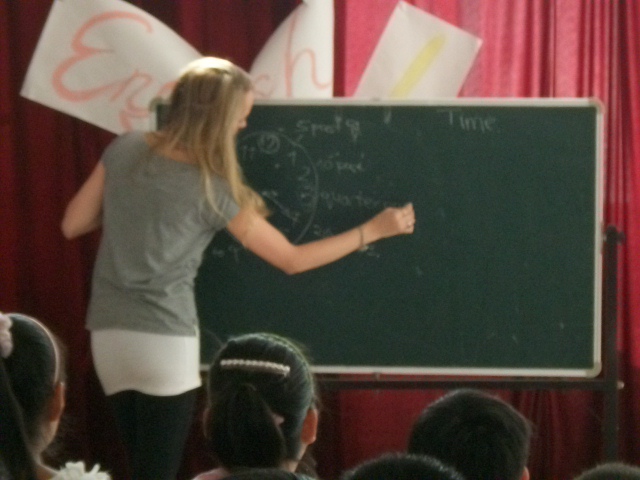 a lady standing at the front of a blackboard writing on it