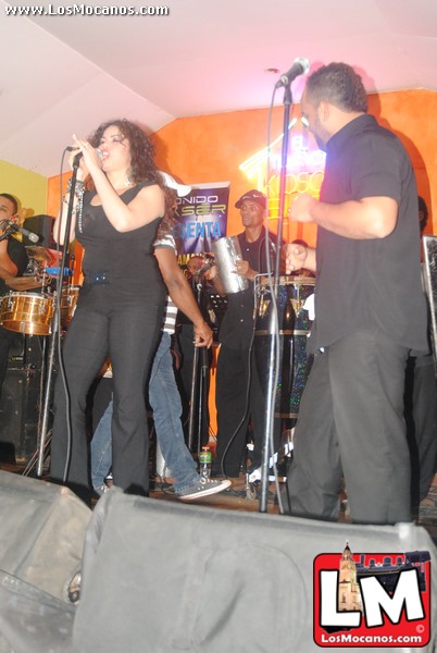 a woman singing on stage with other people watching