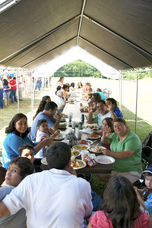 a group of people sit at a table eating lunch under a tent