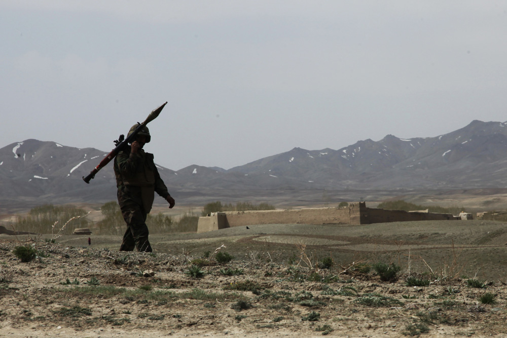 a man with his rifle standing in a field with mountains