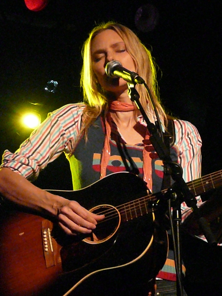 a woman singing into a microphone while playing the guitar