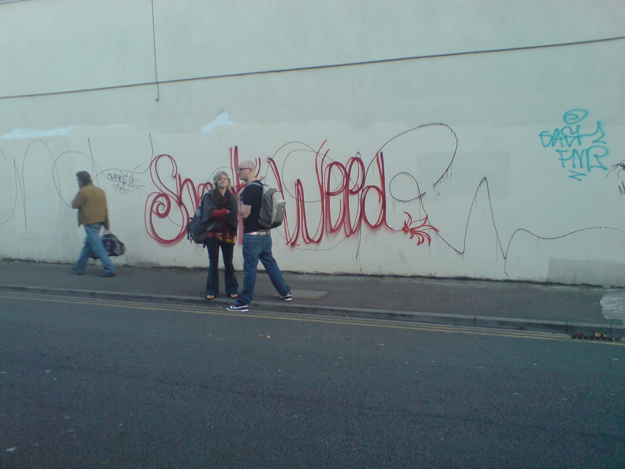 people are walking by a graffiti covered wall