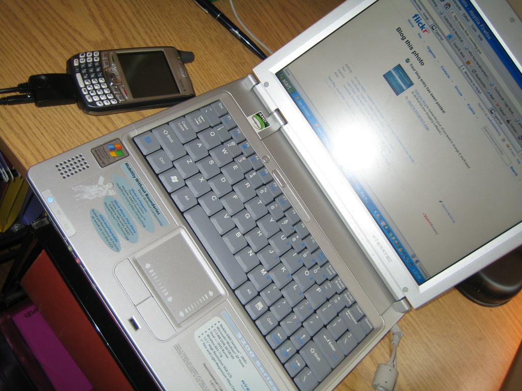 a laptop sitting on a wooden desk with a cell phone and a computer