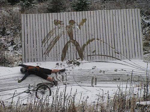 person in black shirt laying on snow covered ground with bike