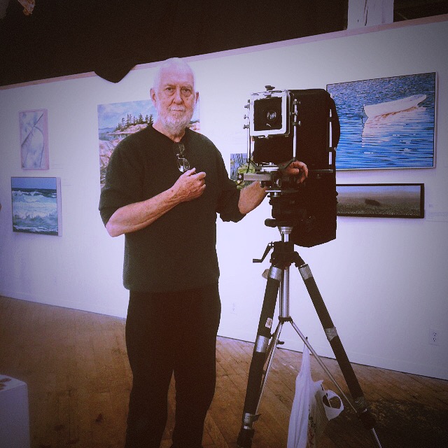 a man holding a camera while standing in front of a painting
