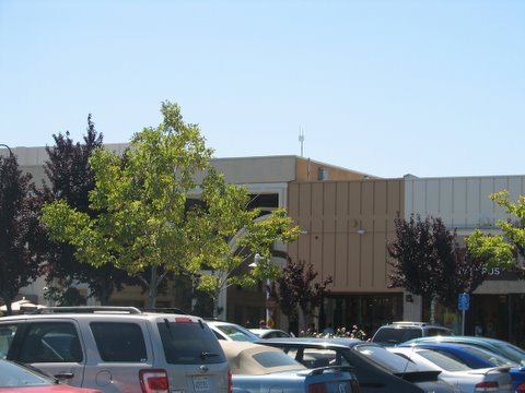 the parking lot full of cars is surrounded by a tan building with a few trees