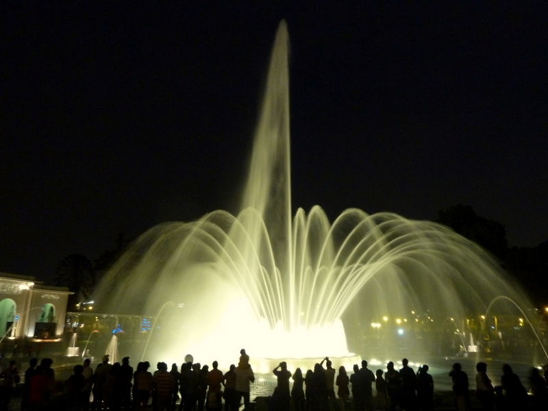 many people in front of a white and water fountain at night