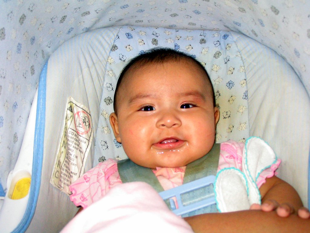 a baby girl sitting in a pink and white crib