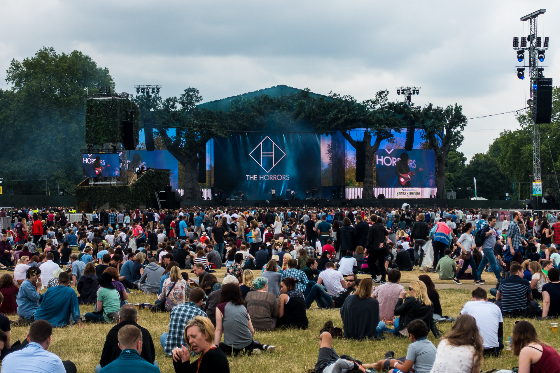 a large crowd sits on the grass near the stage for an outdoor concert