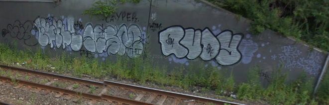a wall with graffiti is next to the train tracks