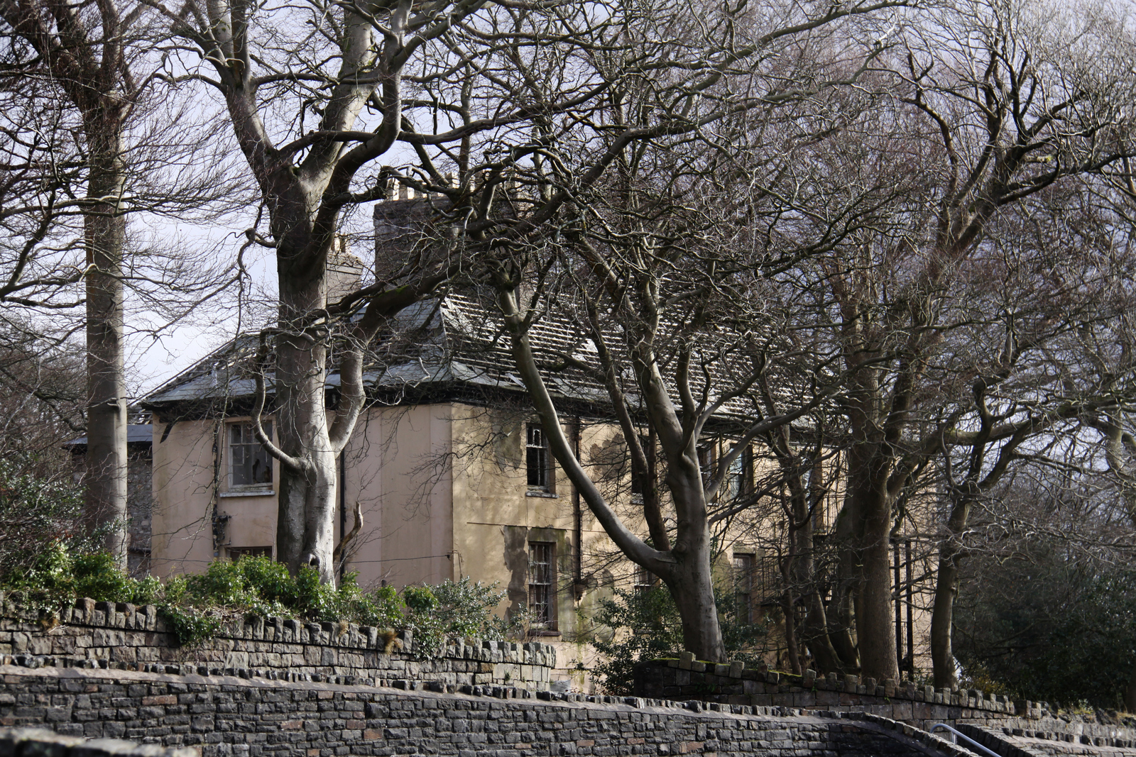a large house next to trees and a stone wall