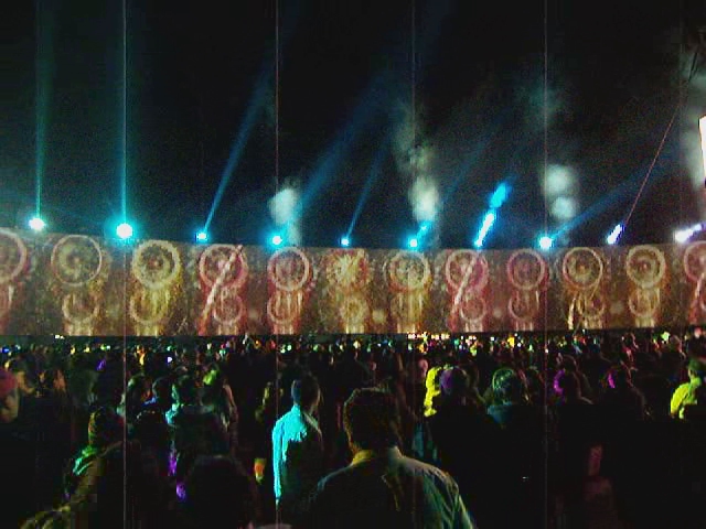 a crowd gathered around some lighting with a large display behind them