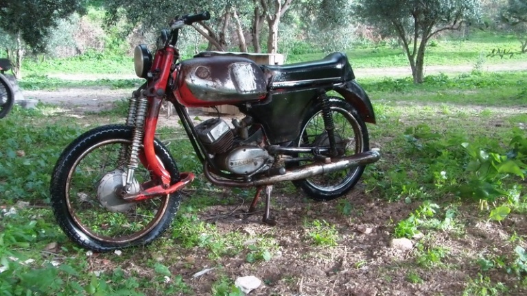 a red motorcycle parked on top of a field next to a forest