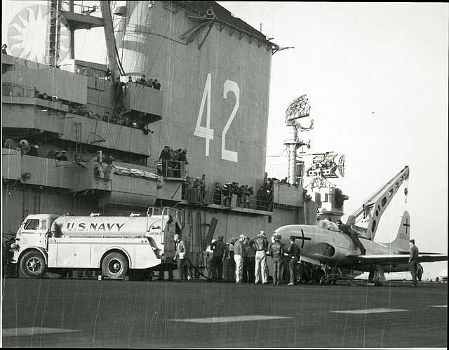 military vehicles lined up with people and a fighter plane